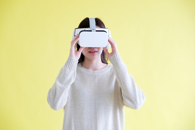 Asian woman wearing virtual reality VR headset while stand over isolated yellow background