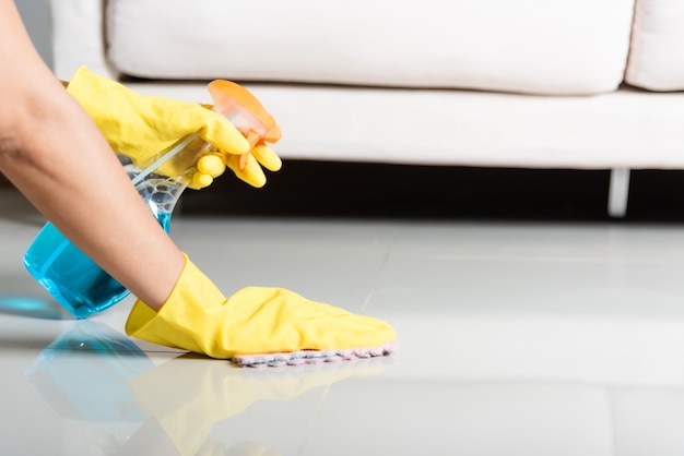 Asian woman wearing yellow rubber glover with cloth rag and detergent spray cleaning floor at home