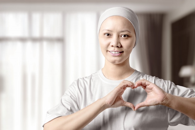 Asian woman in a white shirt showing a heart sign with her hands on the home