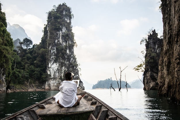 Foto una donna asiatica in camicia bianca siede davanti a una barca con una bellissima montagna in mezzo al mare durante un viaggio in thailandia. incredibile thailandia