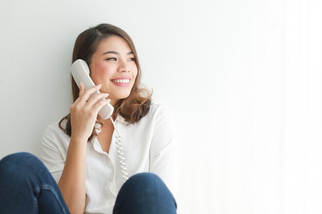 Asian woman in white shirt using vintage telephone talking, in living room