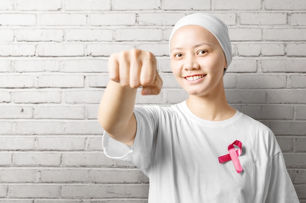 Asian woman in a white shirt with a pink ribbon over a white wall