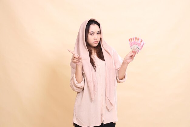 Photo asian woman with angry expression at the camera hand pointing to the right and carrying rupiah money