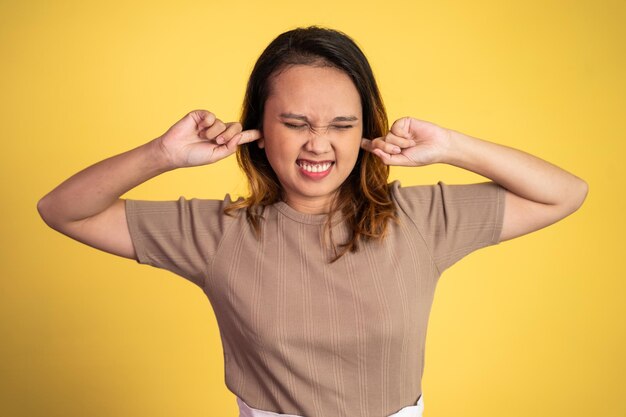 Asian woman with annoyed expression covering ears with both hands on isolated background person