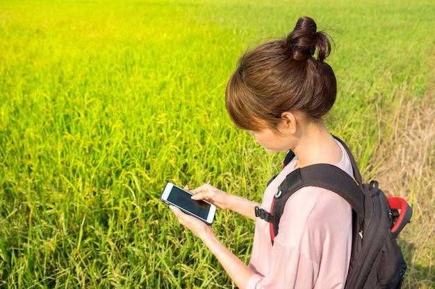 Asian woman with backpack use smart phone outdoor at rice field background