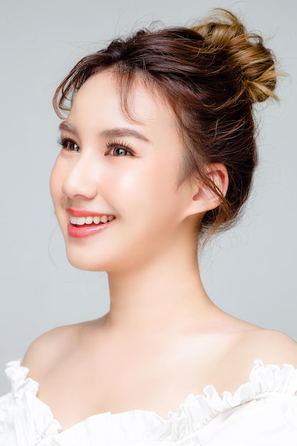 Asian woman with a beautiful face and Perfect clean fresh skin Portrait of female model with natural makeup and sparkling eyes on Grey isolated background Cosmetology Body care plastic surgery