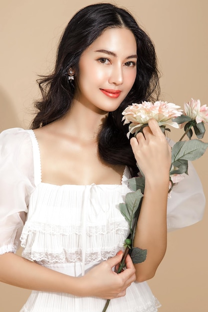 Asian woman with a beautiful face and Perfect clean fresh skin with flower Cute female model with natural makeup and sparkling eyes on beige isolated background