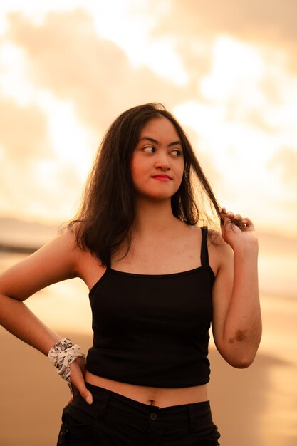 An Asian woman with black clothes and long black hair standing on the beach sand with a flat expression while on vacation