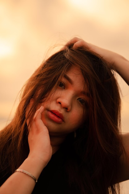 An Asian woman with blonde hair is posing by holding her head on the beach