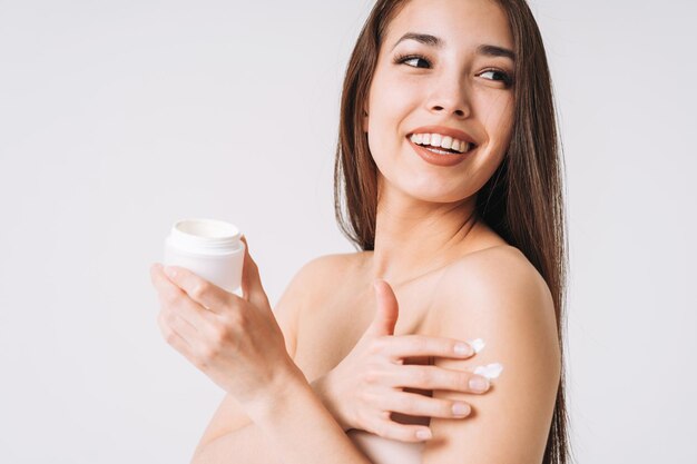 asian woman with dark long hair put day nourishing moisturizer cream on clean fresh skin face