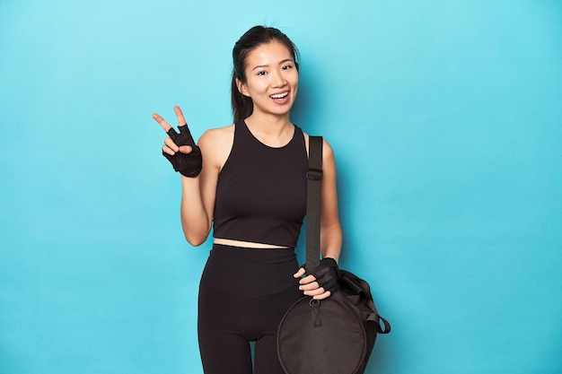 Asian woman with gym gear ready for workout session joyful and carefree showing a peace symbol