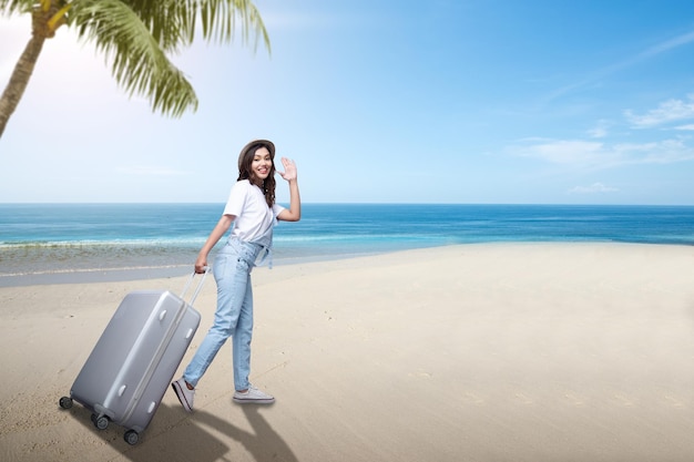 Asian woman with a hat and carrying suitcase on the beach