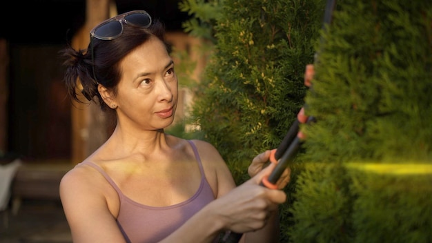 Foto donna asiatica con tagliasiepi che taglia il riflesso della lente del cespuglio verde