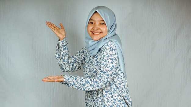 Asian woman with hijab stand and pointing finger standing over gray background