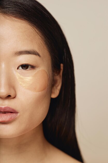 Азиатская женщина с гидратирующими повязками на глазах с половиной лица
