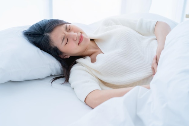 asian woman with a menstrual problems young woman with stomach ache lying on bedlying in bed and holding her stomach