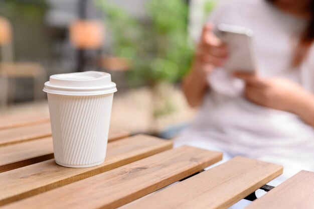 携帯電話と一人でコーヒーを飲むアジアの女性。休日には植物園でリラックスしてレクリエーションを楽しめます。