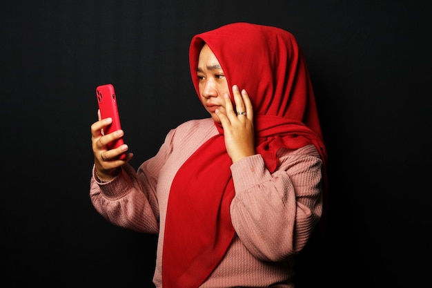 黒の背景に分離された彼女のスマート フォンを見ながら悲しそうな表情でアジアの女性