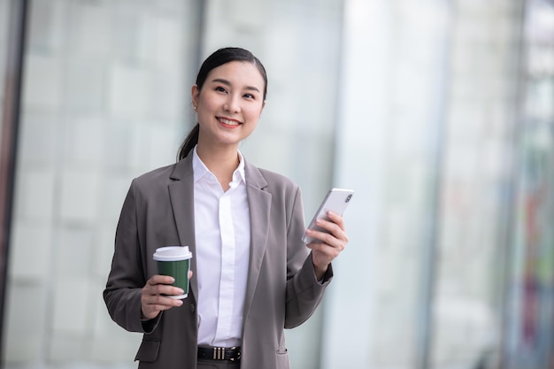 Foto donna asiatica con smartphone in piedi contro la strada sfocata sullo sfondo dell'edificio, fashion business ph