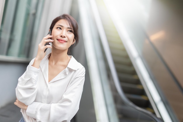 Asian woman with smartphone standing against street blurred building background Fashion business