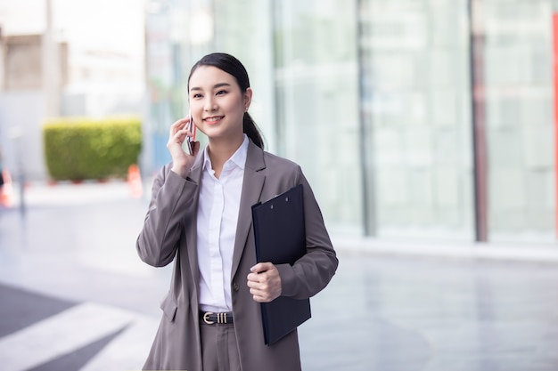 Asian woman with smartphone standing against street blurred building background.
