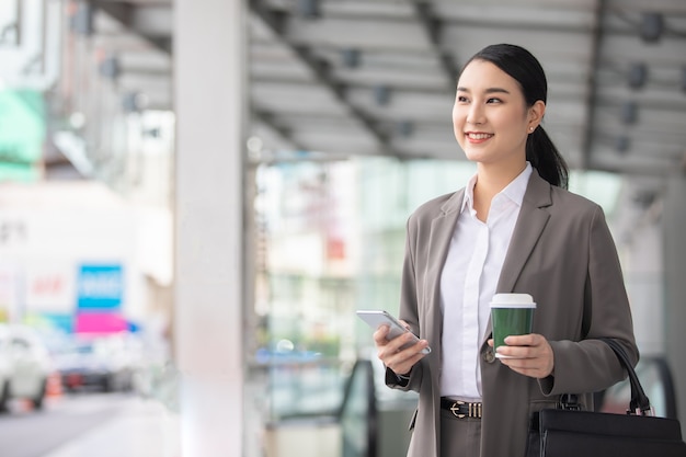 Asian woman with smartphone standing against street blurred building background