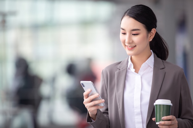 Asian woman with smartphone standing against street blurred building