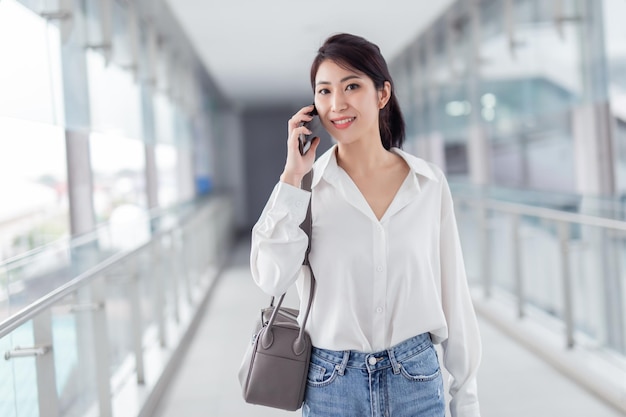 Asian woman with smartphone walking against street blurred building background Fashion business