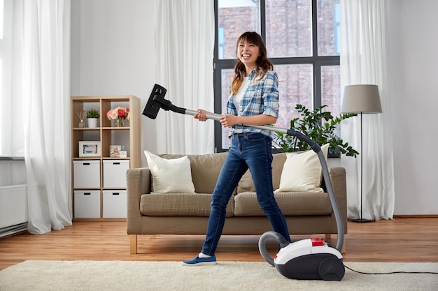 Asian woman with vacuum cleaner having fun at home