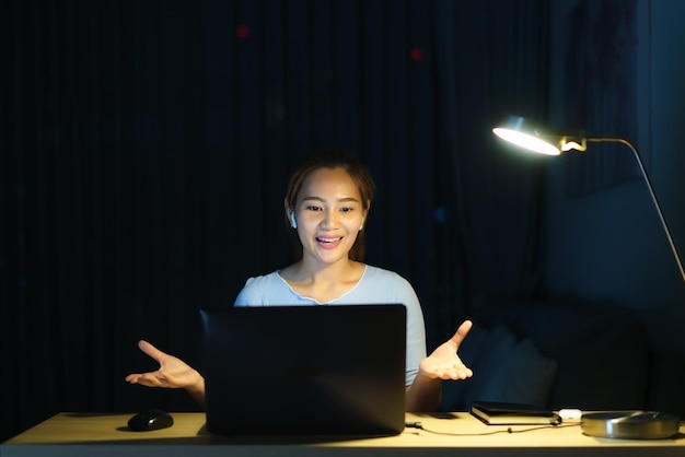 写真 自宅で仕事をしているアジアの女性は、自宅で夜にビデオ通話を介して同僚やマネージャーと一緒に仕事に座っていますxd
