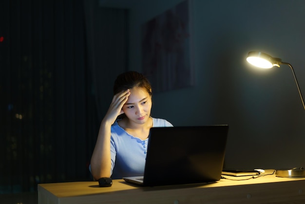 사진 아시아 여성은 사무실 번아웃 증후군 개념에서 노트북 컴퓨터나 노트북에 대한 프로젝트 연구 문제로 스트레스를 받는 밤 늦게까지 일합니다.