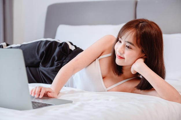 La donna asiatica lavora online e si rilassa in camera da letto a casa. distanziamento sociale e nuovo stile di vita normale.