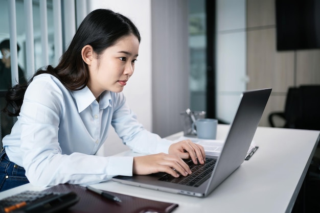 ラップトップ コンピューターを使用して働くアジアの女性手キーボードで入力オフィスで働くプロの投資家が新しいスタートアップに取り組む