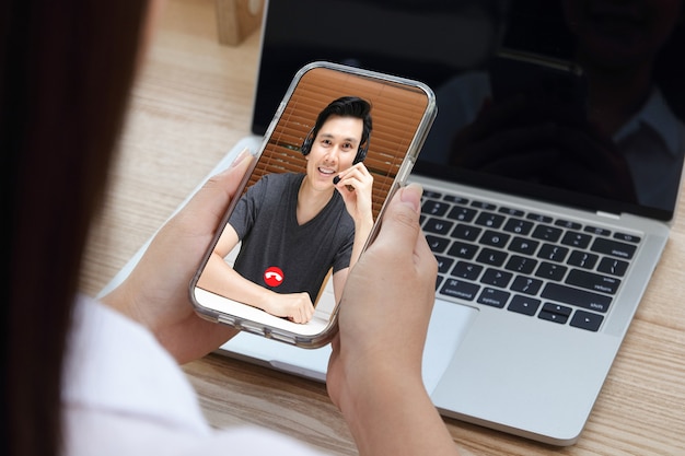 Foto donna asiatica che lavora da casa sta facendo una videochiamata online sul suo smartphone per discutere di lavoro. concetto di distanza sociale moderna tecnologia di comunicazione