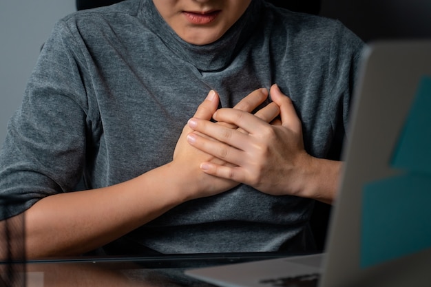 La donna asiatica che lavorava su un laptop era malata di dolore al petto seduto in ufficio