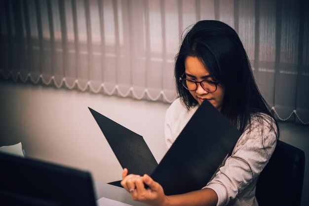 オフィスで働くアジアの女性若いビジネスウーマンは、deskthailandの人々にたくさんのファイルで仕事の過負荷からストレスを感じました