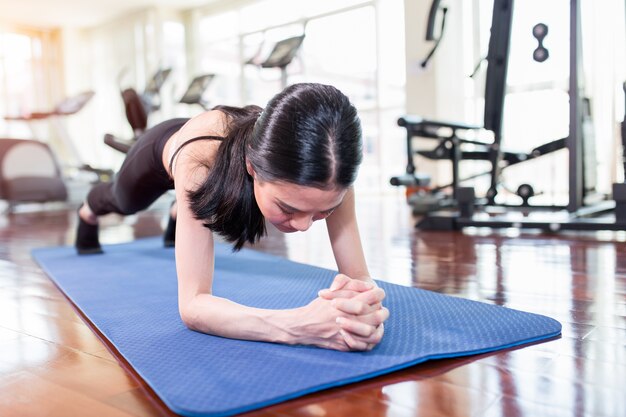 La donna asiatica che risolve nella palestra e che fa l'yoga si esercita sulla stuoia blu.