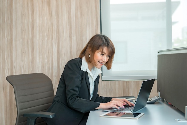 オフィスで残業しているアジアの女性ビジネスマンたくさんの仕事ラップトップでファイルをチェックタイの人々はオフィスの制服を着ています