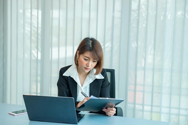 オフィスで残業しているアジアの女性ビジネスマンたくさんの仕事ラップトップでファイルをチェックタイの人々はオフィスの制服を着ています