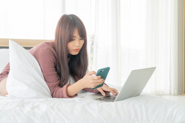 Donna asiatica che lavora con il computer portatile sul letto