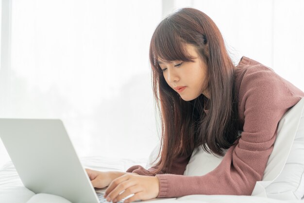 ベッドの上のラップトップで働くアジアの女性