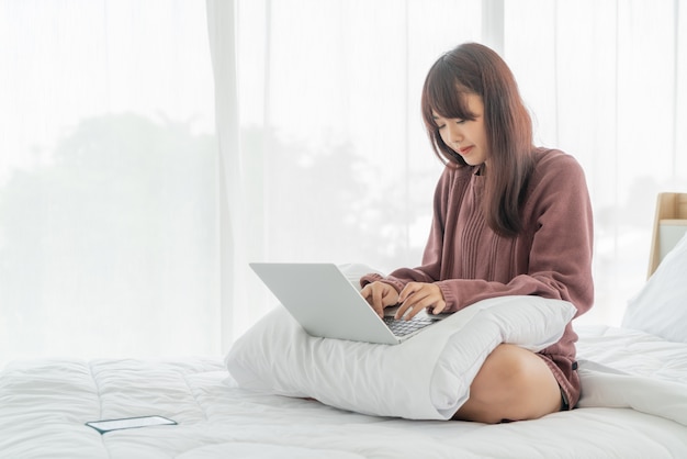 ベッドの上のラップトップで働くアジアの女性