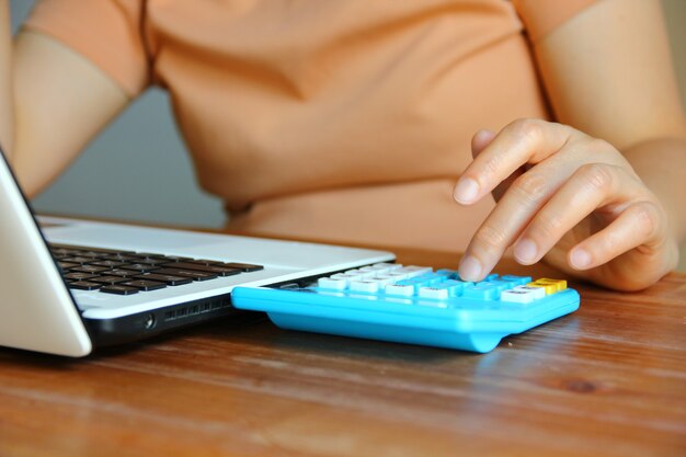 Asian woman working with laptop while left hand using calculator