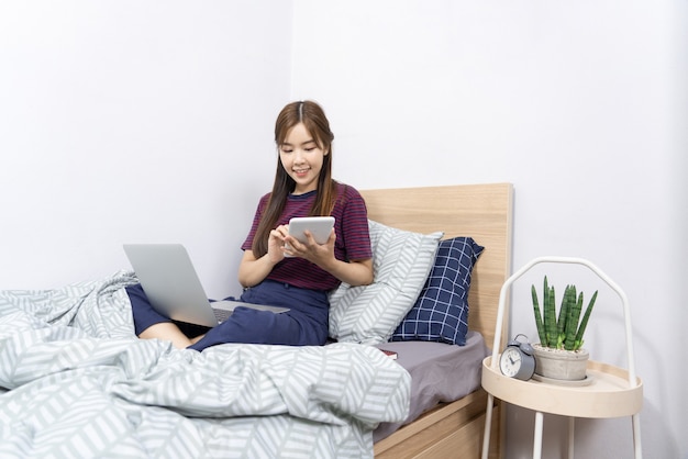 Asian woman working with smartphone or tablet on bed at home