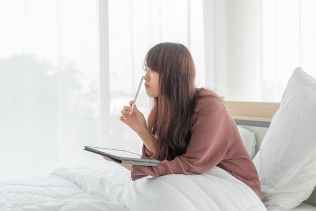 Asian woman working with tablet on bed