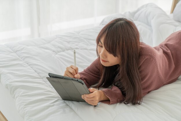 Asian woman working with tablet on bed