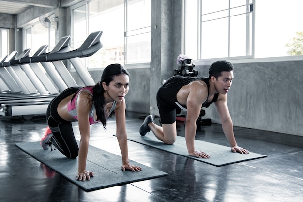 asian woman workout lower thigh on a yoga mat with trainer man at the gym. Concept of exercise in gym. Woman and man workout on yoga mat.