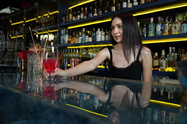 Photo asian woman works as a bartender standing the counter holding a stainless steel shaker and mi