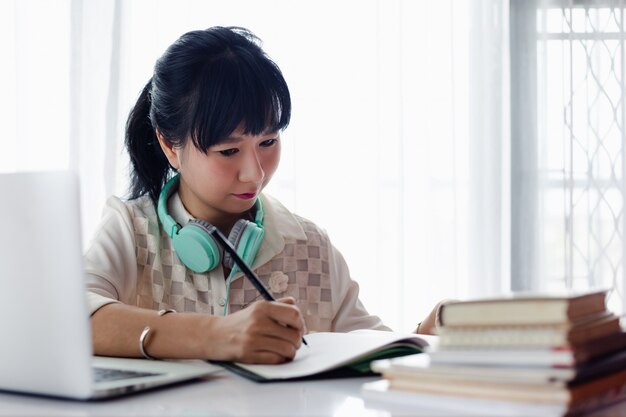 Asian woman writing on the paper, using laptop and working at home for business, self-quarantine, staying home and social distancing in coronavirus or covid-2019 outbreak situation concept