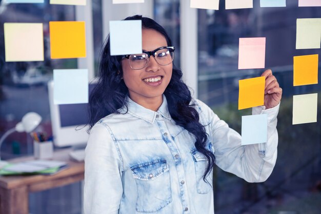 Asian woman writing on sticky notes on glass wall